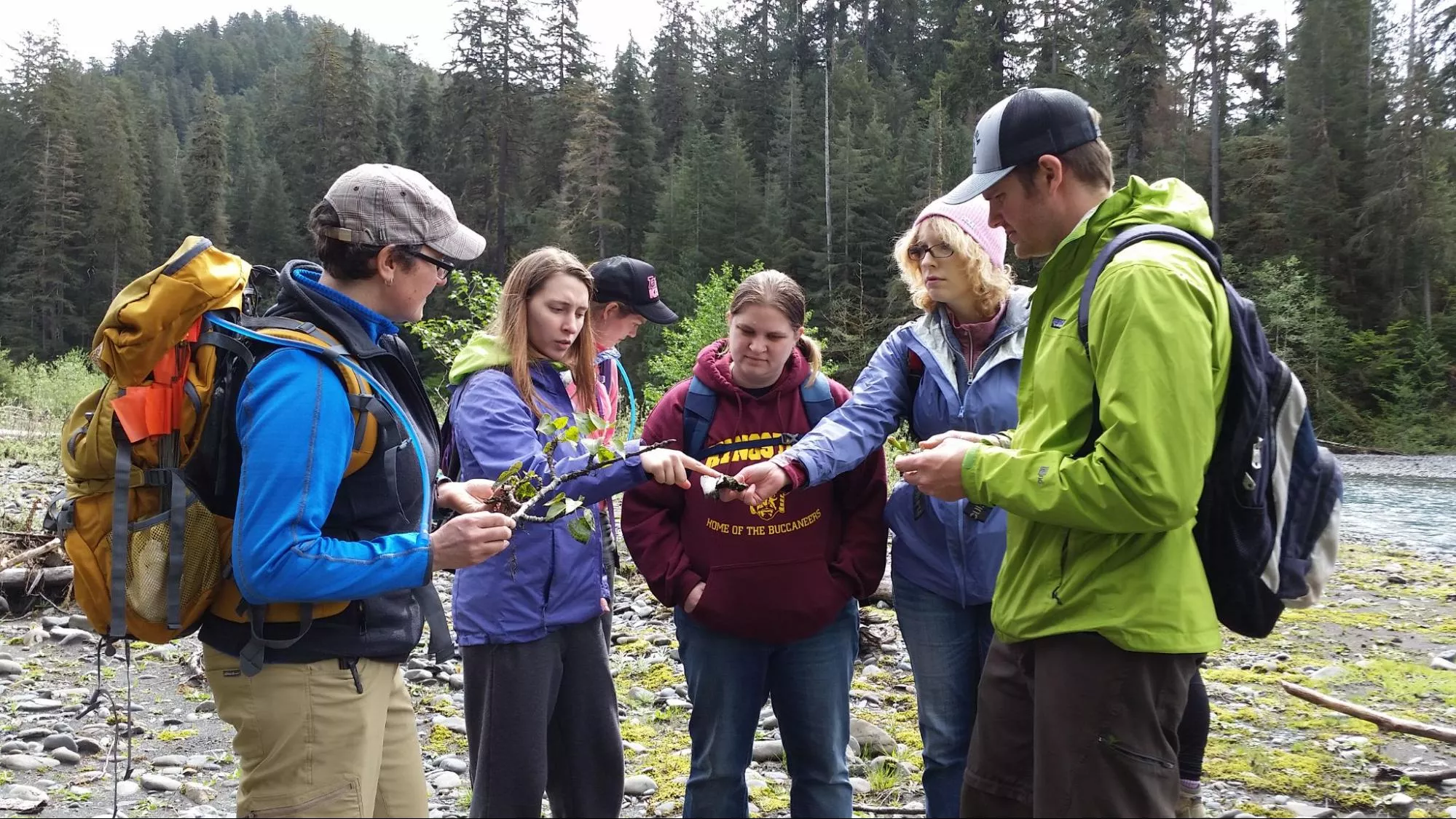 Group of students standing by a river investigating and discussing branch samples