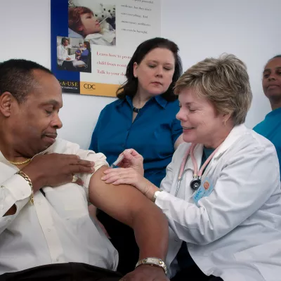A doctor giving a man a shot, while two nurses look on