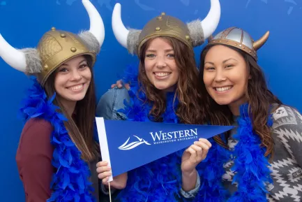 Three Western Students smiling, wearing viking helmets and holding a Western flag