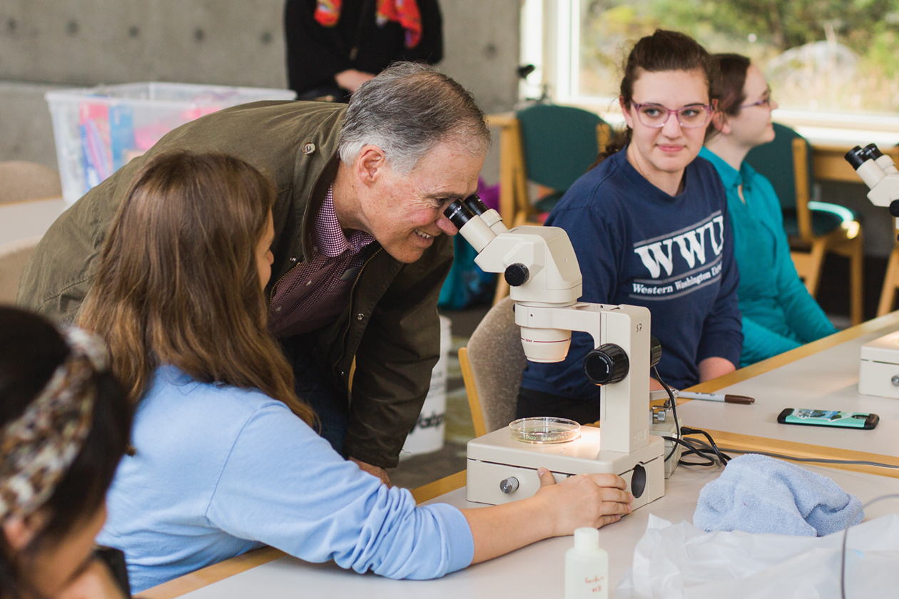 Governor Jay Inslee looking through a microscope with nearby students
