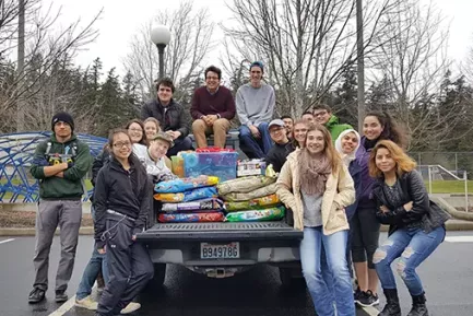A group of students and faculty gathered around the back of a pick up truck full of bags of dog food