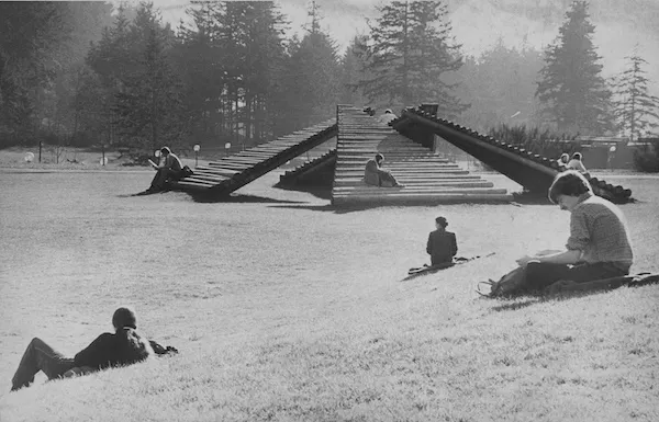 Black and white photo of students lounging in front of log sculpture